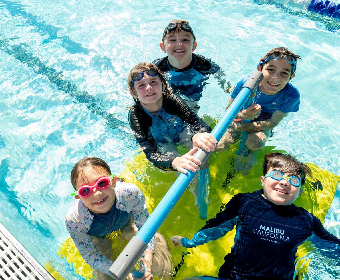 an image of children in the pool swimming and smiling at the camera