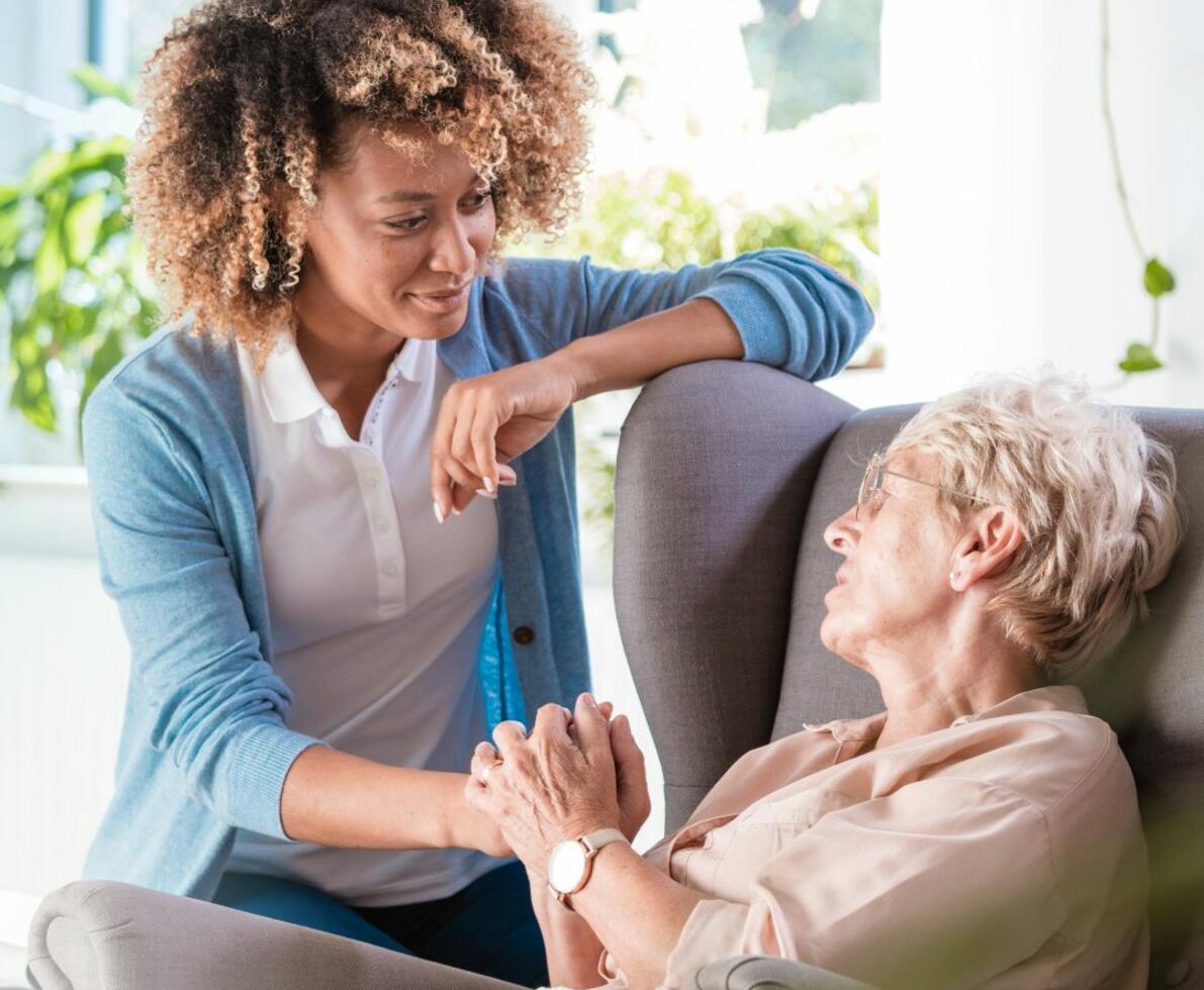 smiling carer sitting with her patient with their hands intertwined together