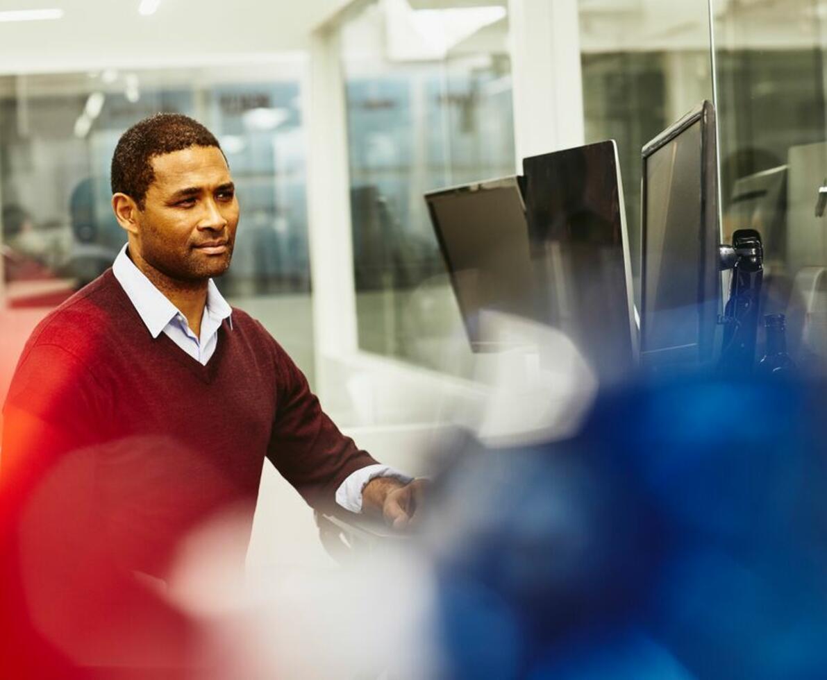 man wearing a maroon sweater looking concerned at a computer 