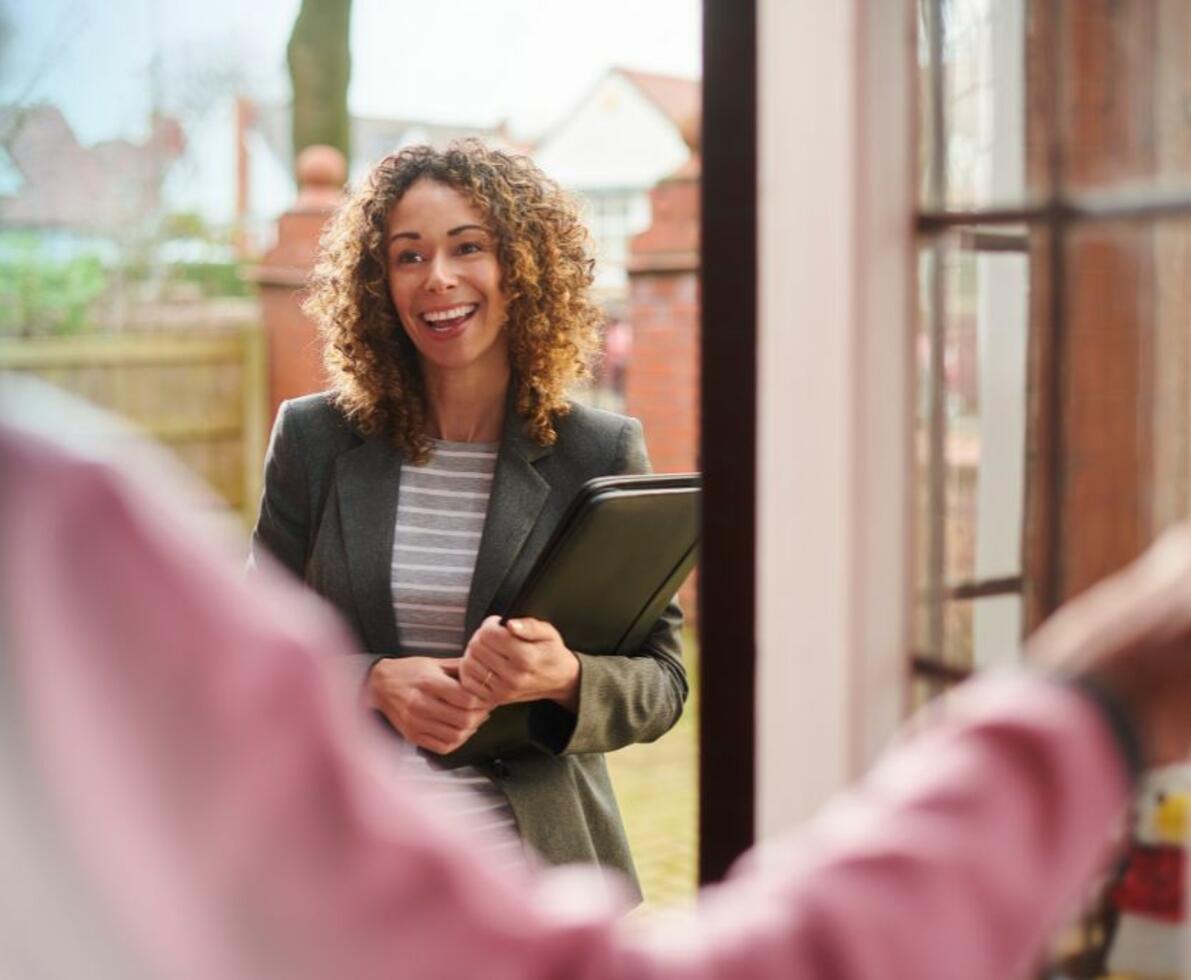 smiling woman standing at residential entryway being greeted by someone at the door