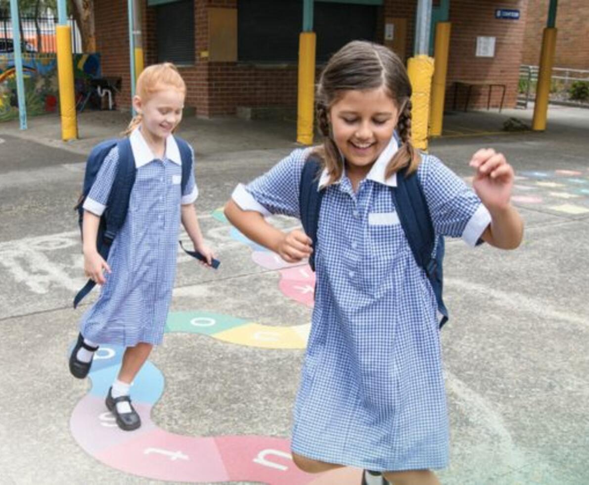 two children in school uniforms playing hopscotch in the schoolyard