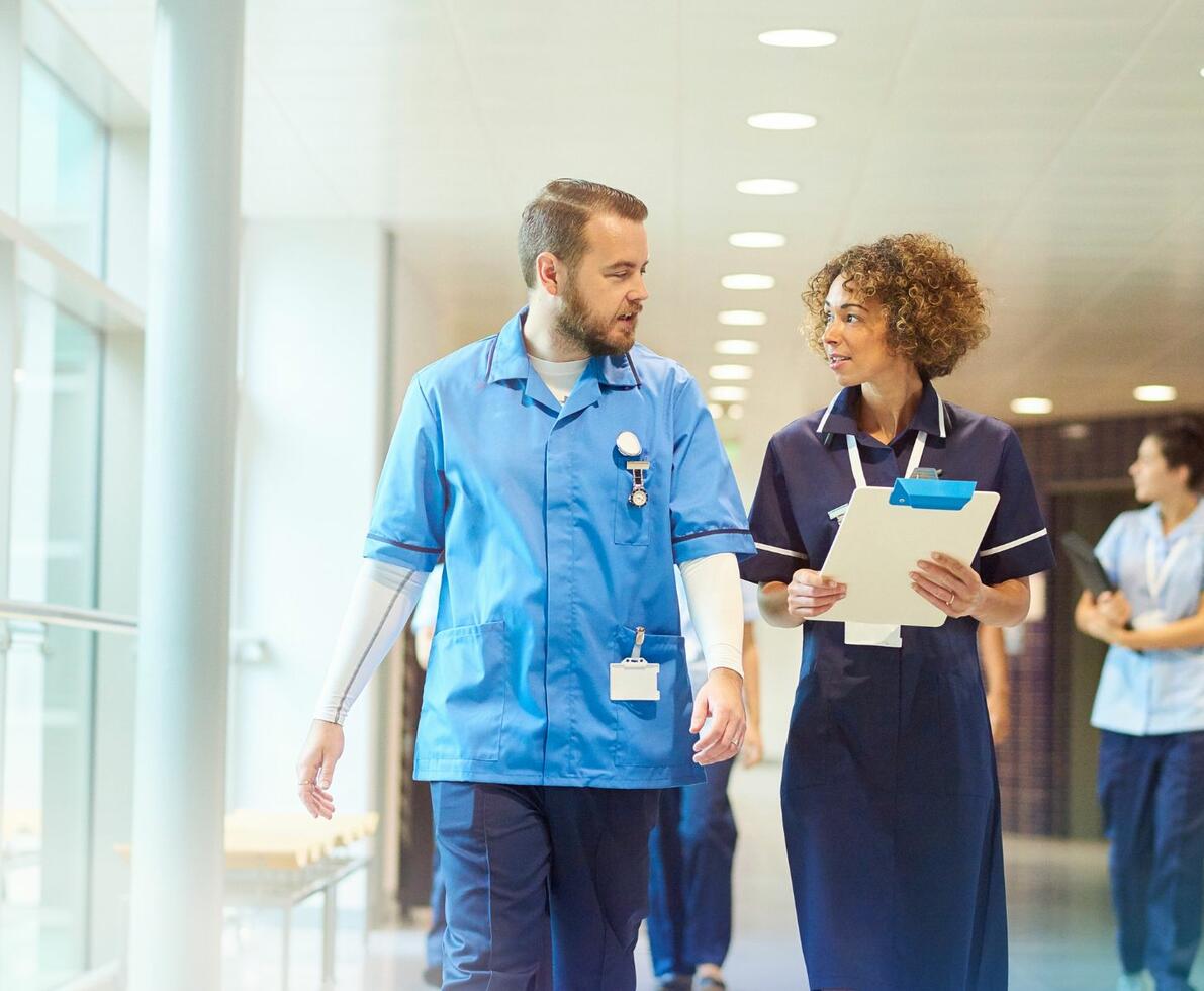 A male and female healthcare professional walking together in a hospital corridor having a conversation
