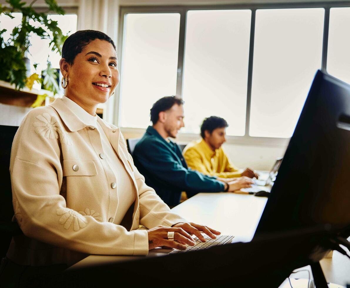 an image of a woman typing on her laptop while smiling brightly and looking at something to her far right 