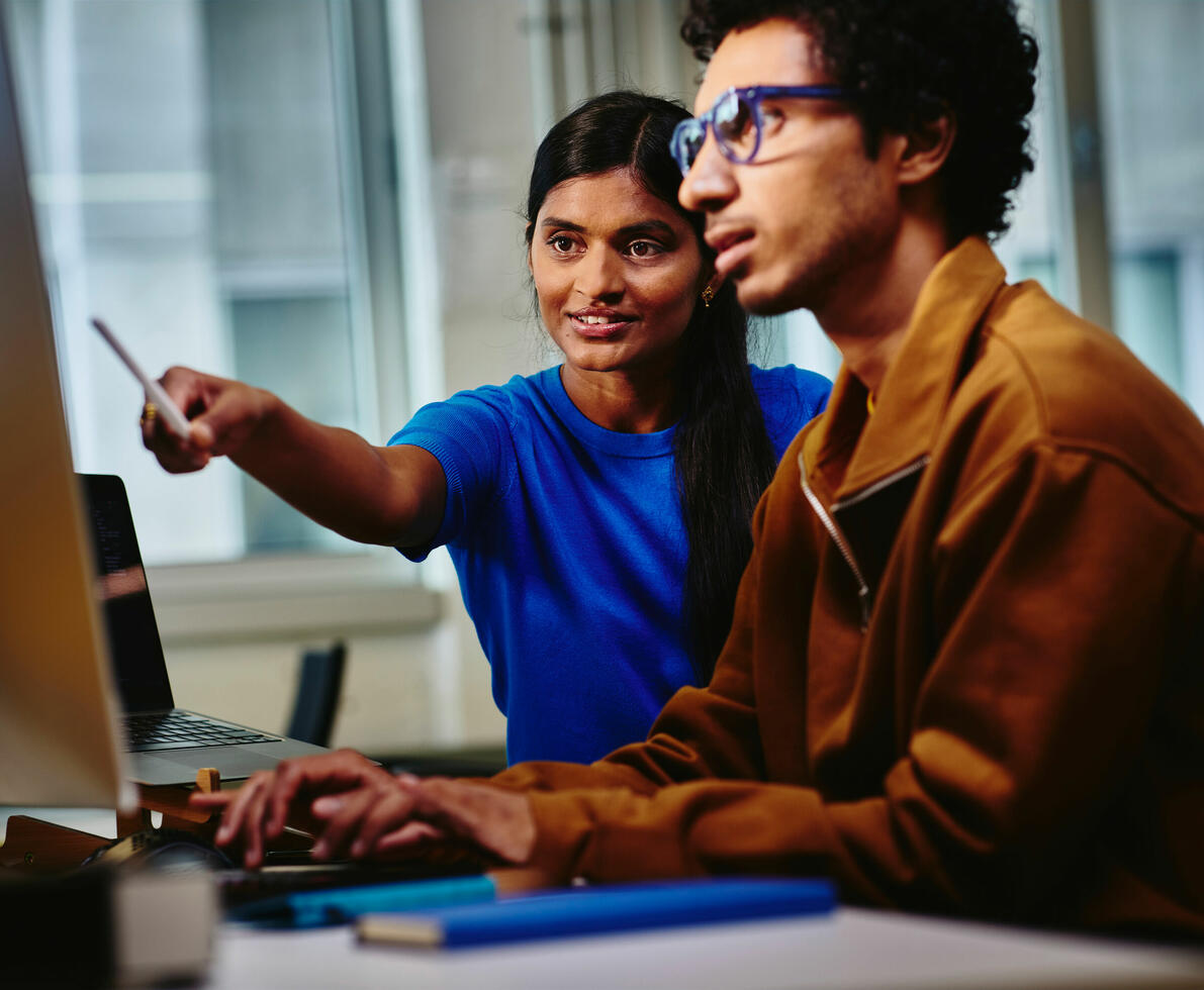 an image of two workers looking at something in the monitor while smiling and working