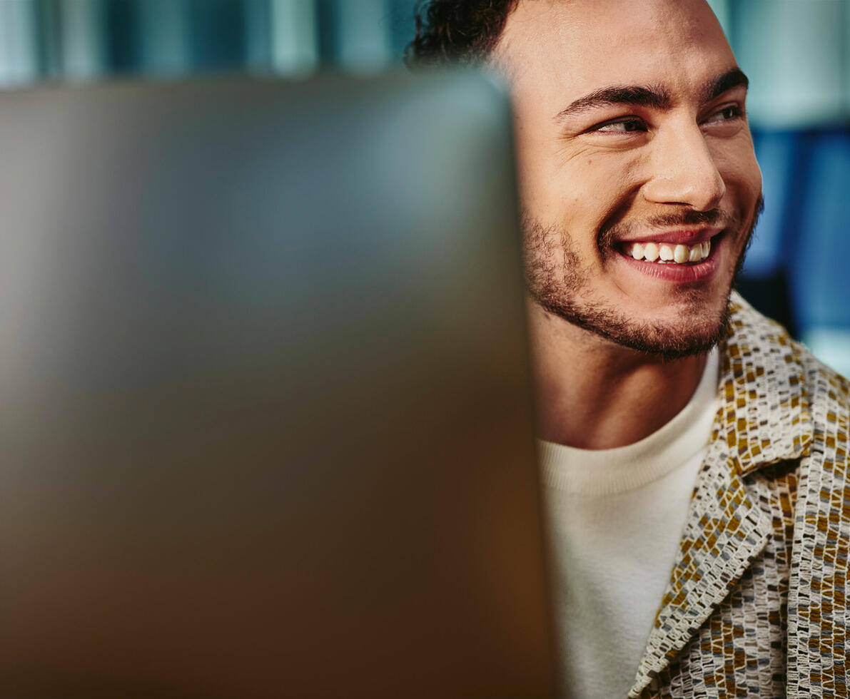 an image of a man looking to the far right smiling brightly while working in front of his laptop