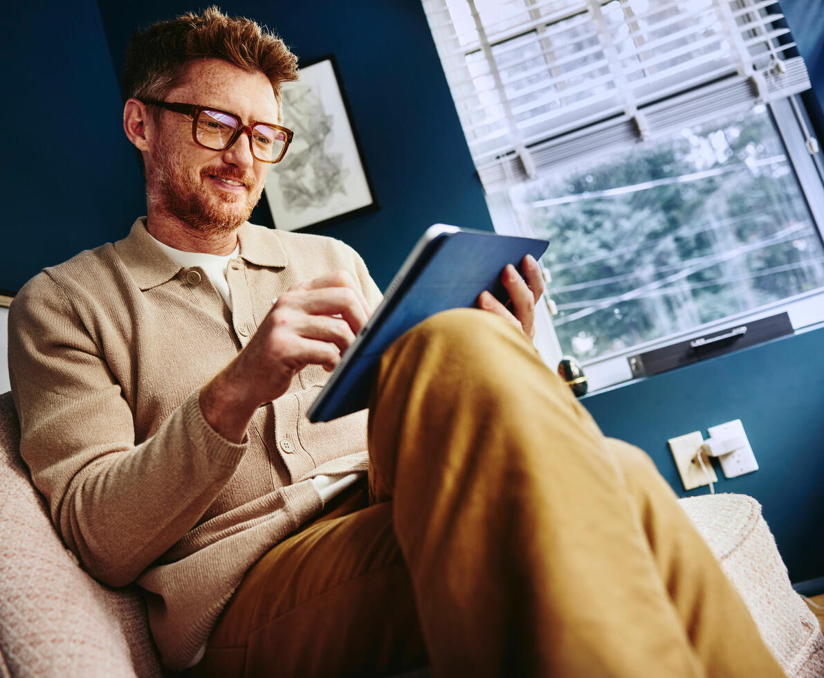 an image of a man wearing glasses and sitting on a chair while using his tablet 
