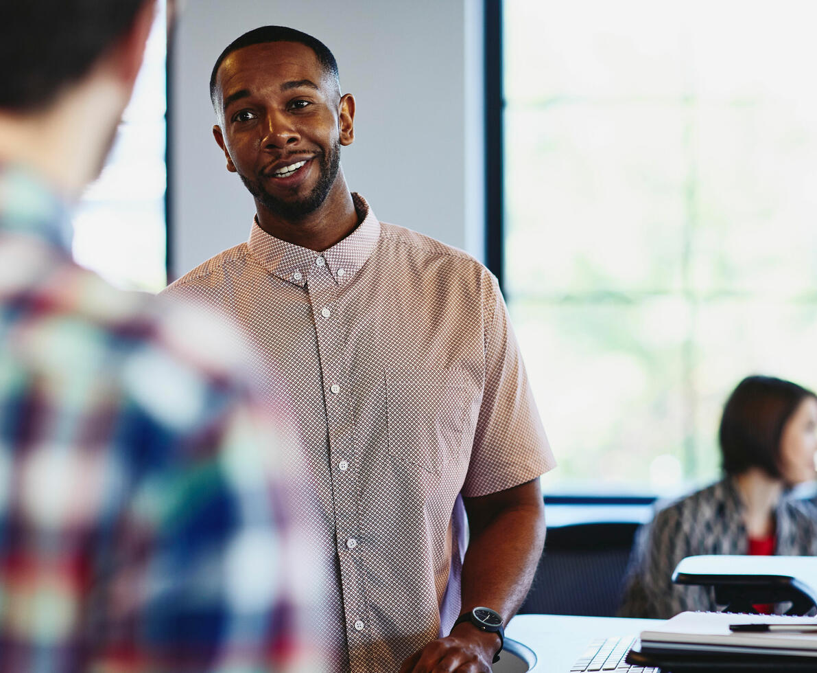 a man talking to his colleague with a woman in the background working