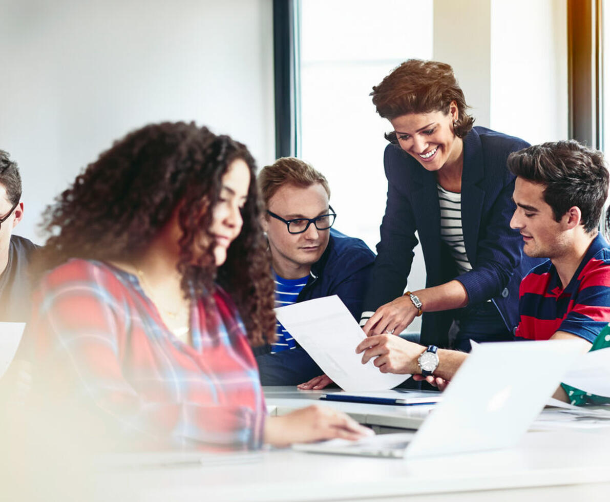 an image of a woman pointing at something on a piece of paper that her students are holding