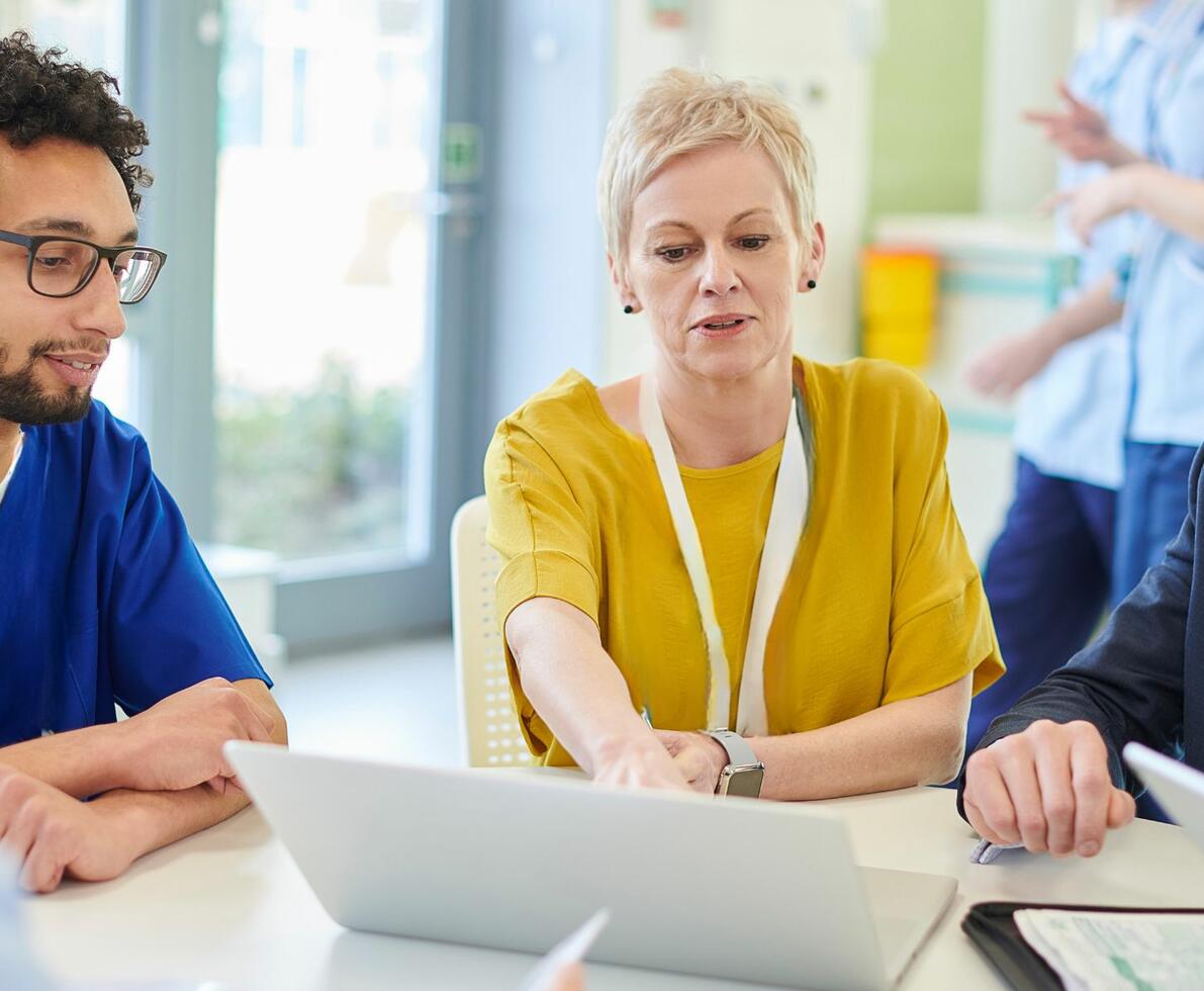 image of a woman in a healthcare facility talking with some colleagues. The male colleague is wearing scrubs
