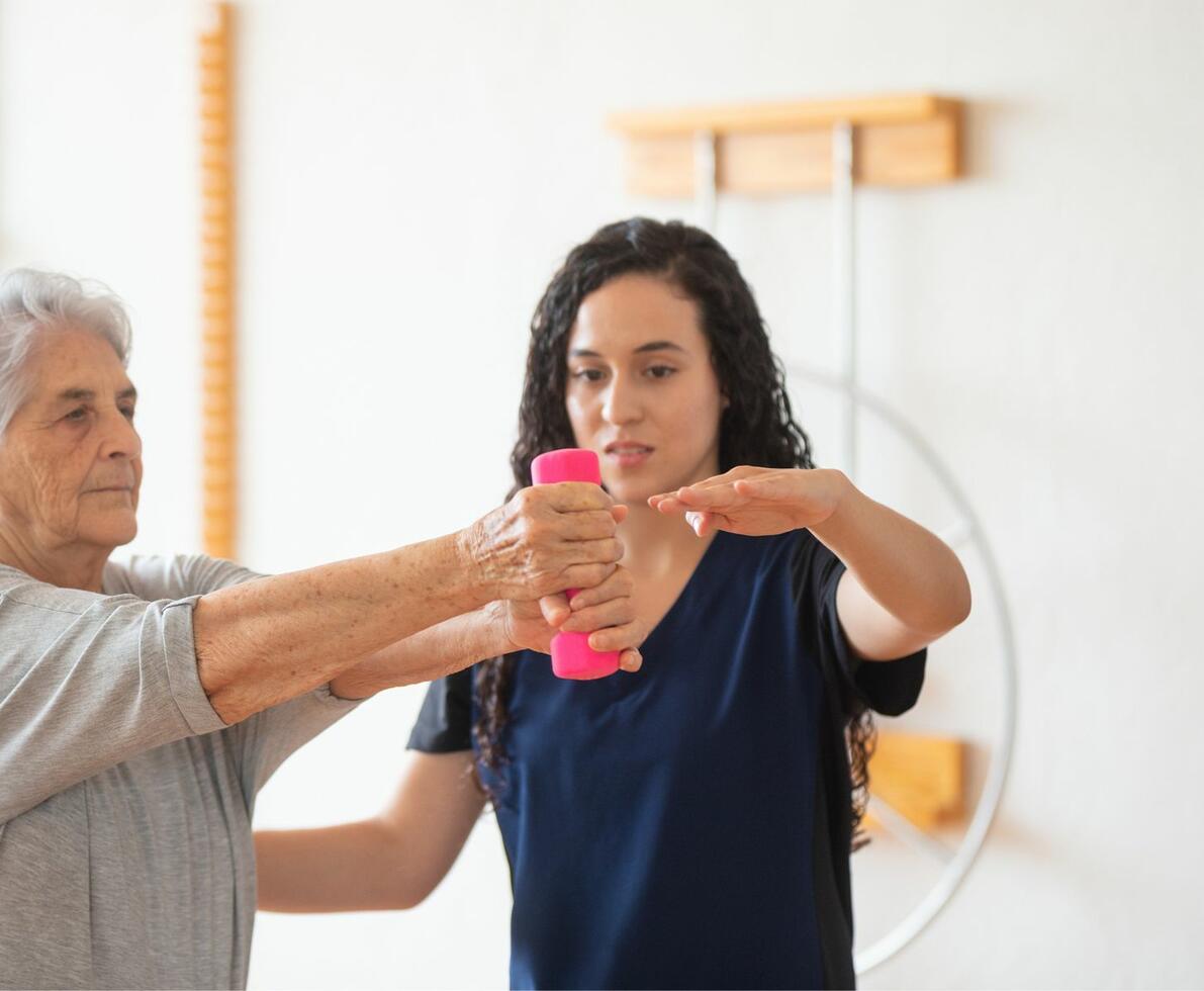 image of a healthcare professional supporting her patient who is holding a weight in her hands