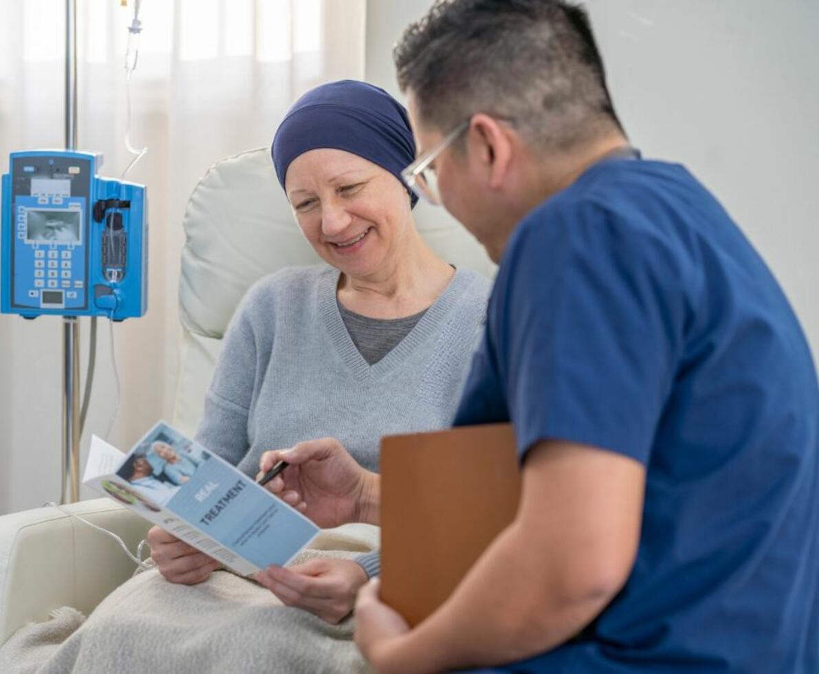 an image of a man wearing scrubs showing a flyer to a woman in a hospital room