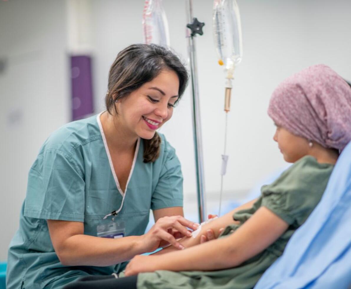 a woman wearing scrubs smiling at a child in a hospital bed