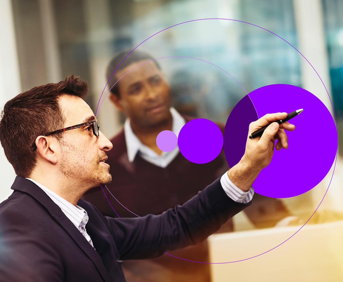 an image of two men working together in an office with one pointing at something on the monitor