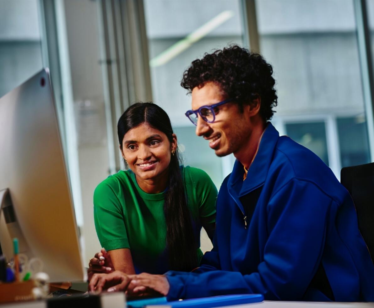 woman and man speaking at a desk in front of a computer 