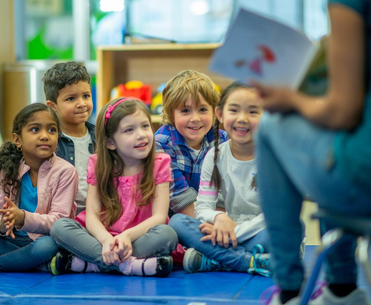 Group of children in a daycare centre. Their teacher is showing them a picture and they are smiling