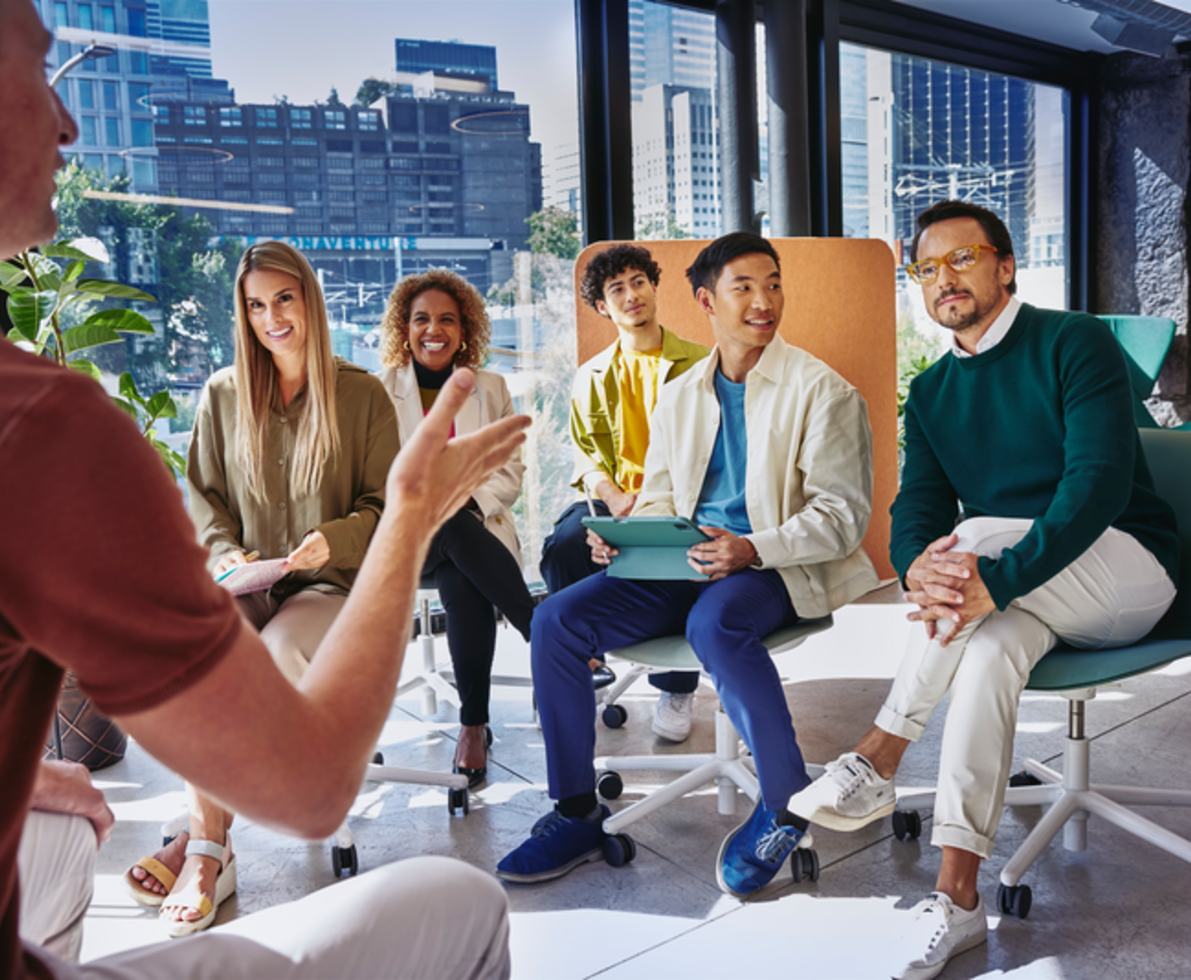 team of 5 people listening to a man presenting in an office with city views 