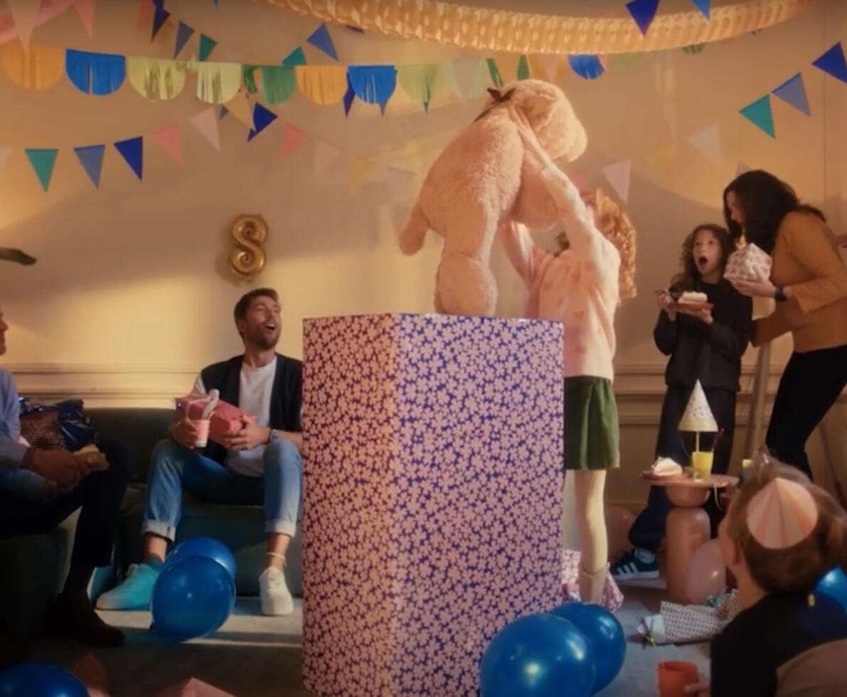 child holding up bear at a party after unwrapping the present, everyone acting surprised