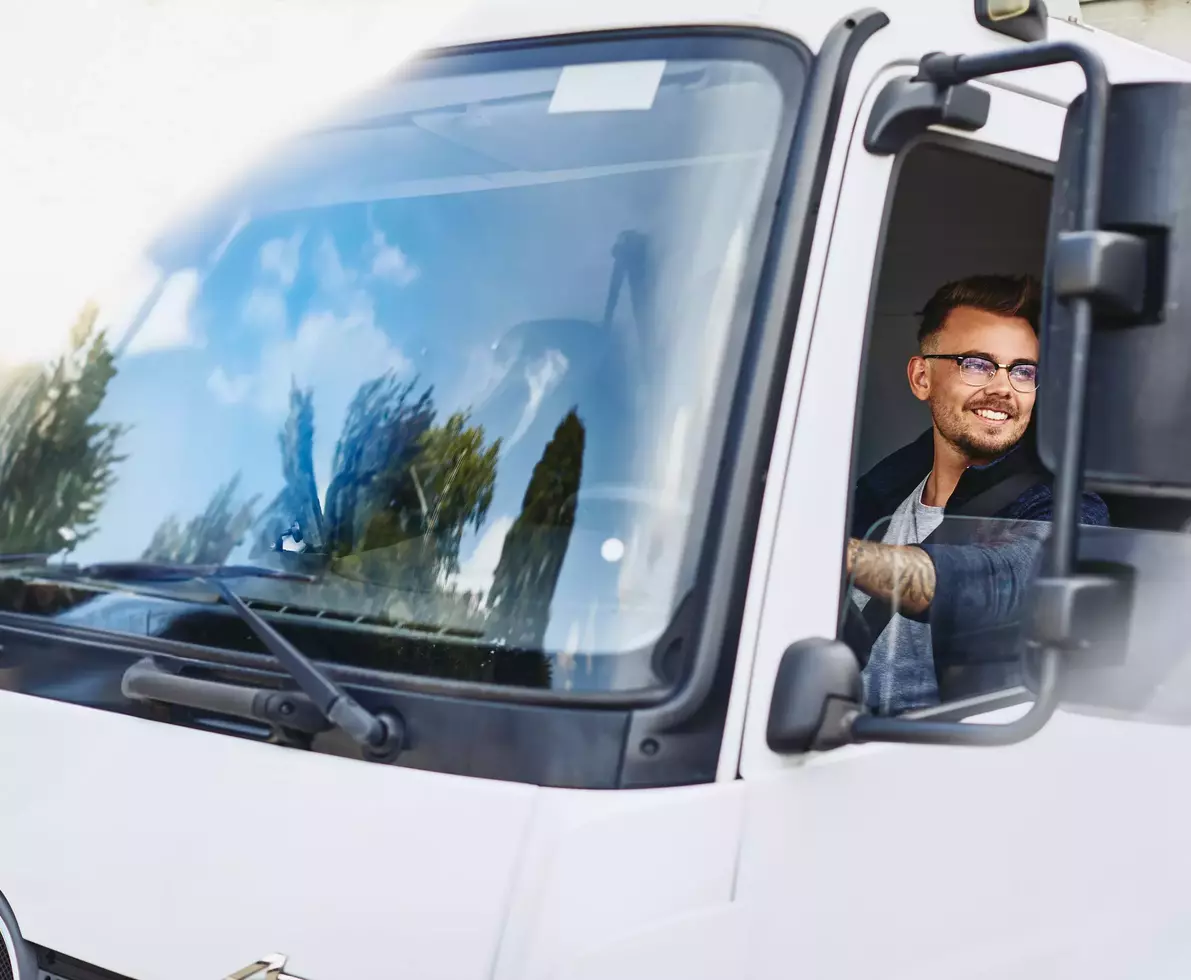 Smiling male wearing glasses driving a truck.
