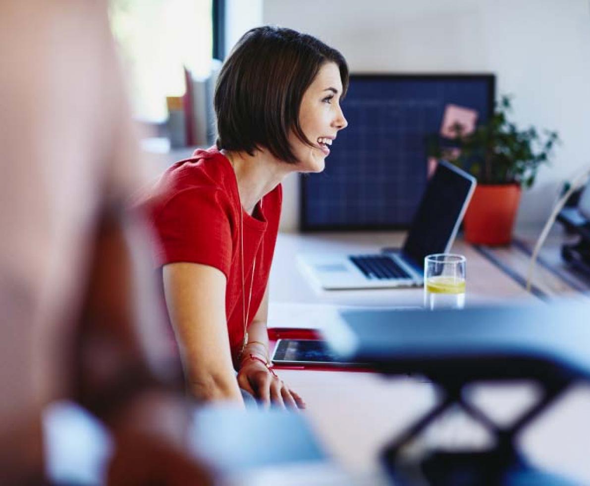 Short-haired woman in red talking with her deskmate