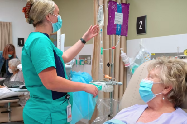 blonde female nurse assisting an older female patient, both wearing masks