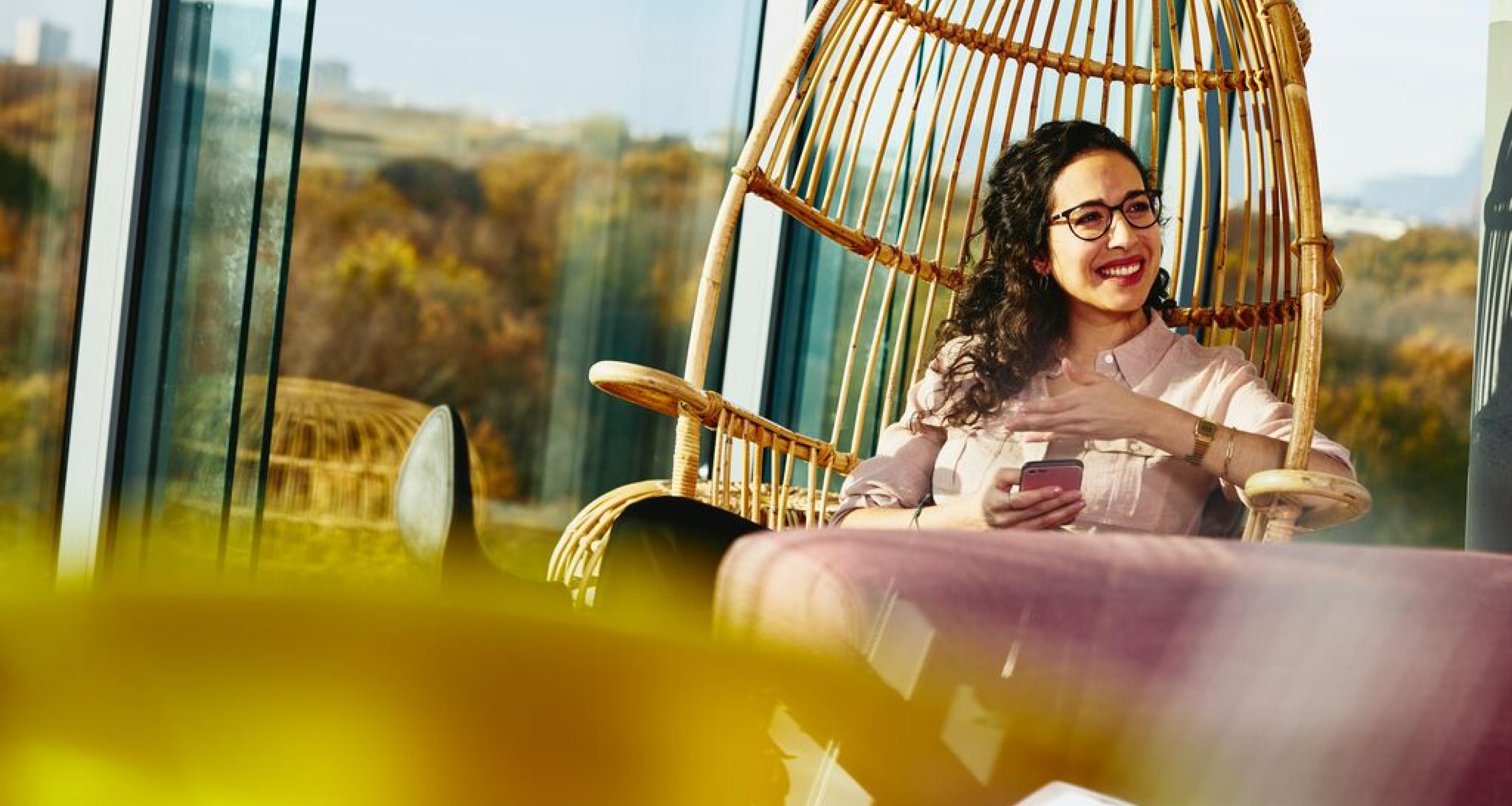 Woman smiling looking away while sitting down and holding her phone.