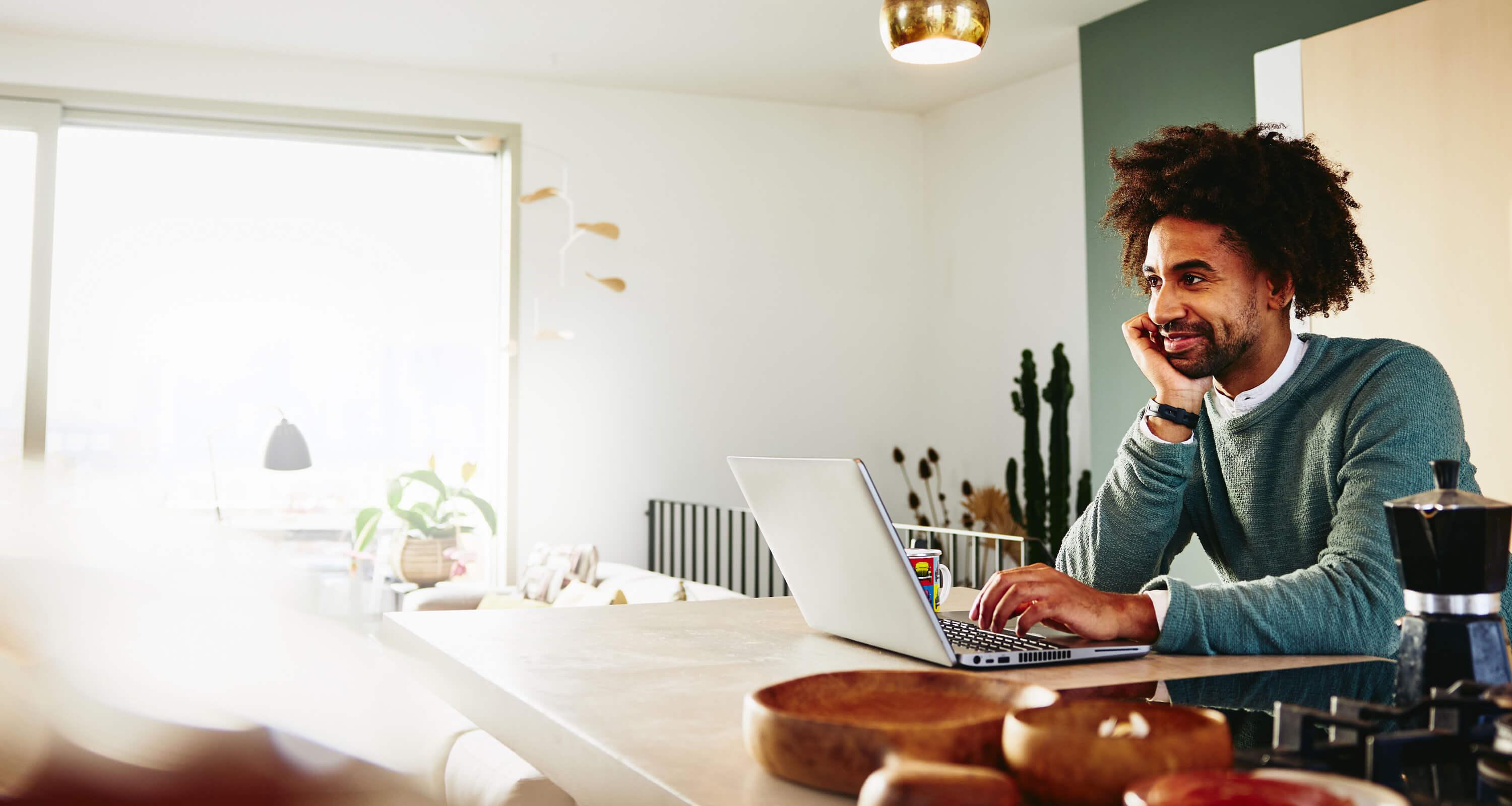  A man with a laptop resting his chin on his palm while smiling at something far away