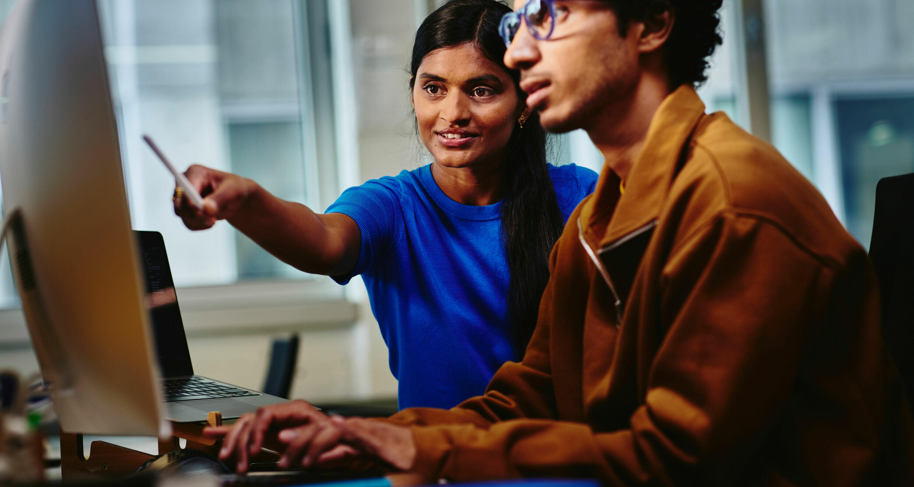 an image of two workers looking at something in the monitor while smiling and working