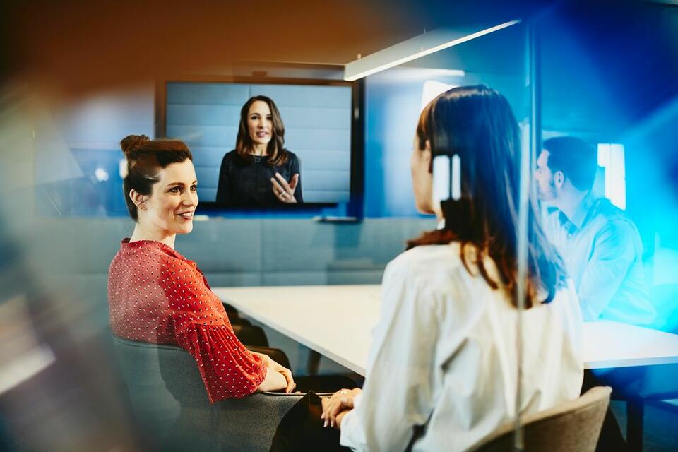 a group of people inside a conference room talking to someone on video call