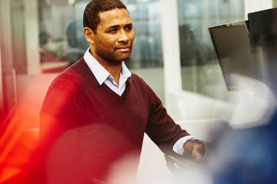 man  in a maroon sweater looking concerned at computer screen while looking at a job scam