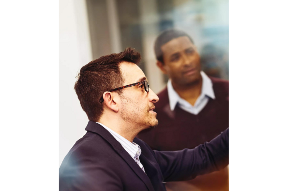 a man pointing at a computer screen for his coworker to see something they are discussing