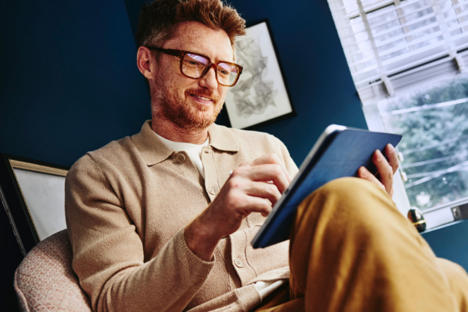 an image of a man wearing glasses looking at his tablet while smiling