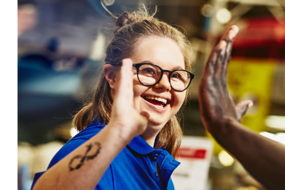 an image of a woman wearing glasses and a blue polo shirt giving her colleague a high-five