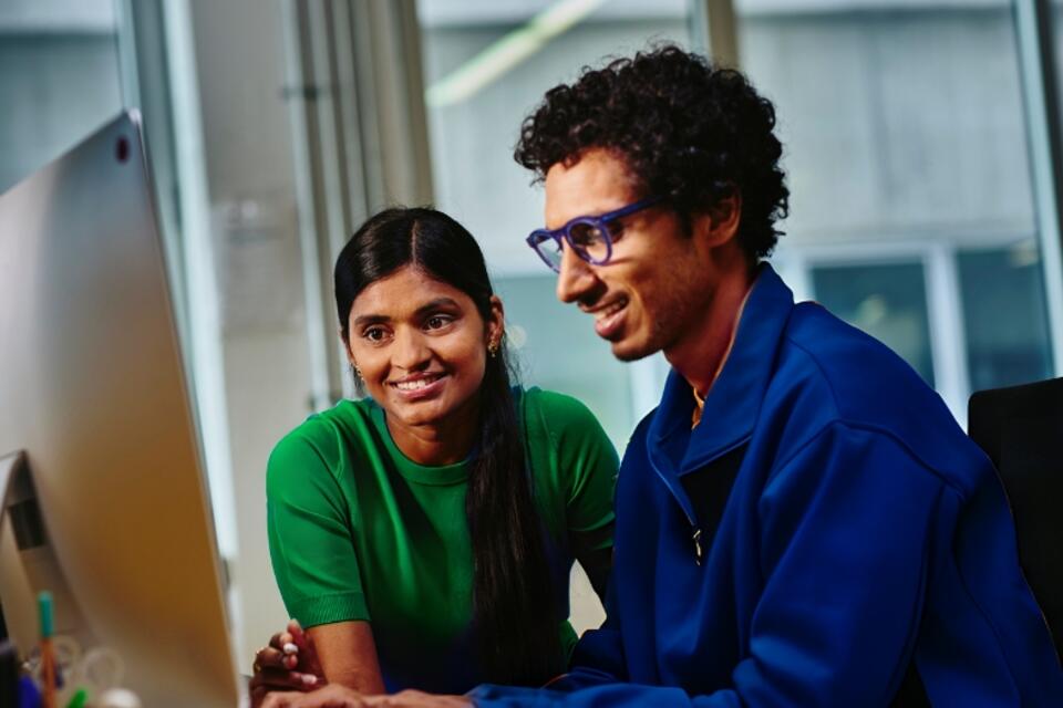 an image of two coworkers smiling while looking at something on the monitor