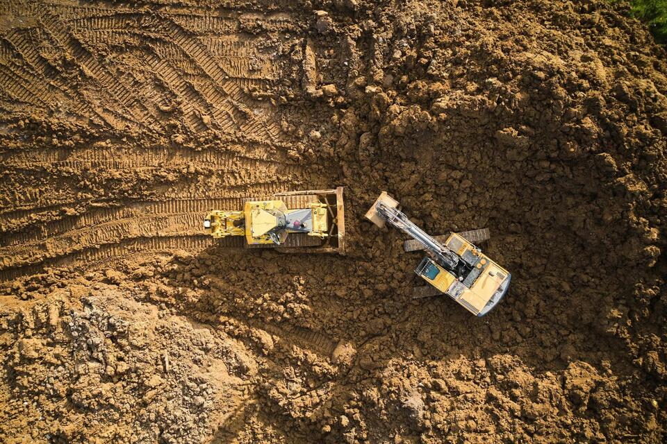 bulldozer is scraping a layer of soil and excavator is digging and dumping dirt