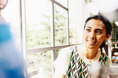 a woman in a colourful top seated by the window while talking to her colleague