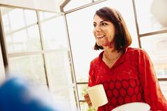 a smiling woman wearing a red top with a cup in her hand