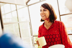 an image of a woman wearing a red blouse and holding a cup smiling while looking to the left