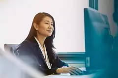 Womale in a black blazer, sitting at her desk.

