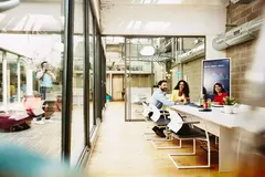 Three colleagues having a meeting in a meeting room, while one colleague is making a call outside the room.
