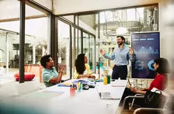 Four colleagues having a meeting in a meeting room. Financial charts in the background.
