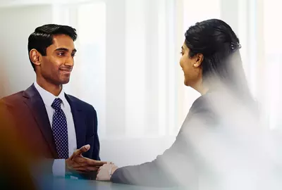 an image of a man talking with a woman while seated in front of her and both wearing a business attire