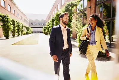 male and female talking and having a laugh while walking outside between office buildings