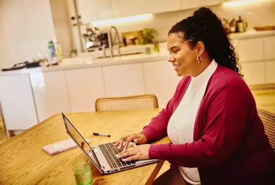 Female, smiling, working on laptop in kitchen on a kitchen table