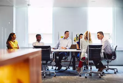 Group of colleagues sitting down in a meeting room at the office, smiling.
