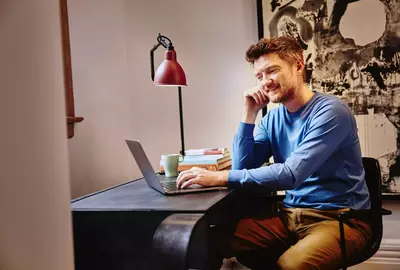 Male in a blue shirt sitting at a desk working on his laptop