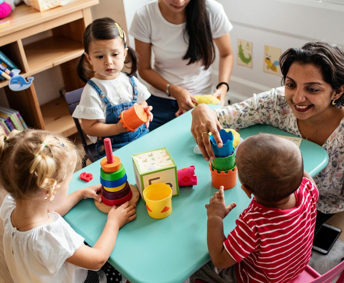 Group of children playing with building blocks in a daycare centre. They are accompanied by their educator.