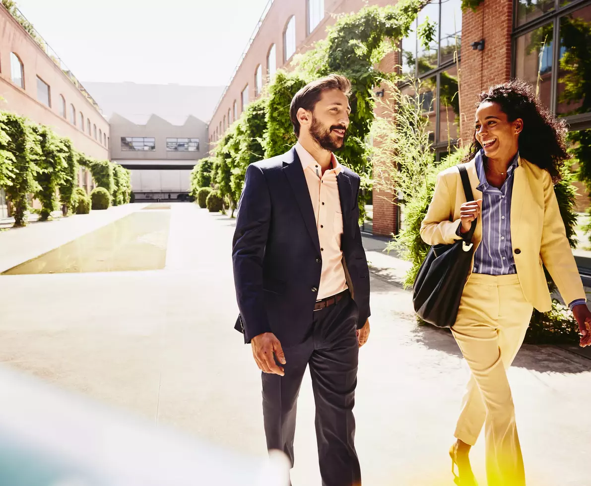 male and female talking and having a laugh while walking outside between office buildings
