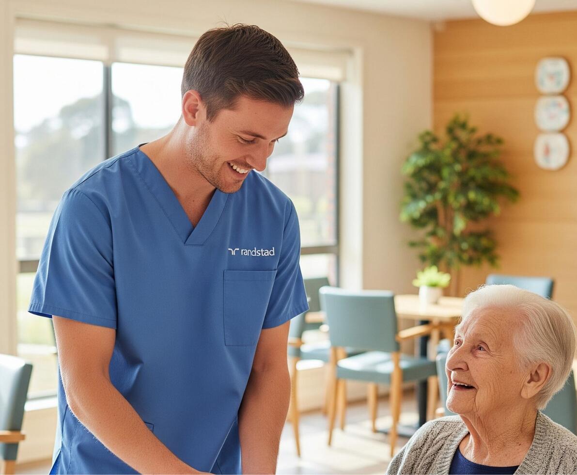 a smiling male aged care professional in a facility with a female resident. The resident is also smiling