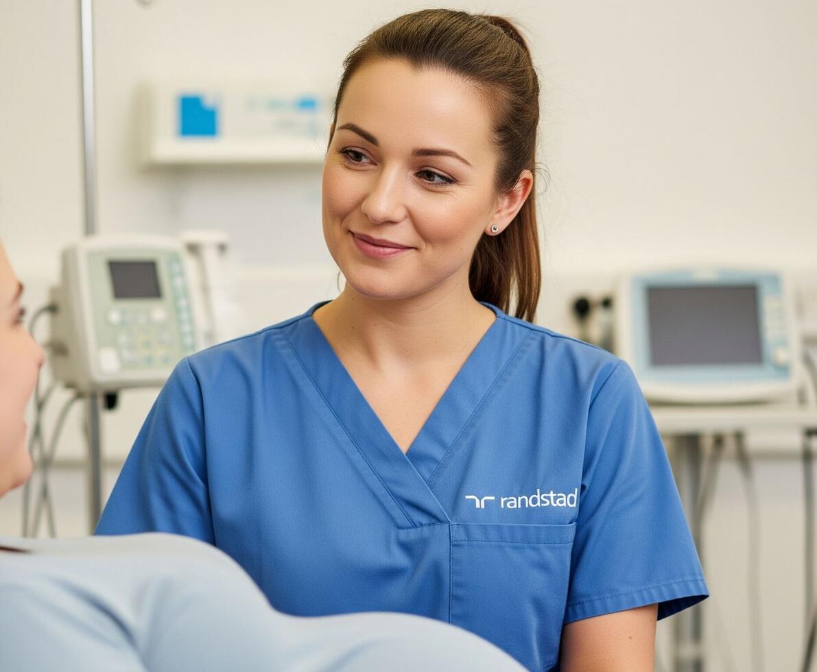 a smiling midwife in a hospital ward talking to a pregnant patient that is sitting up in a hospital bed