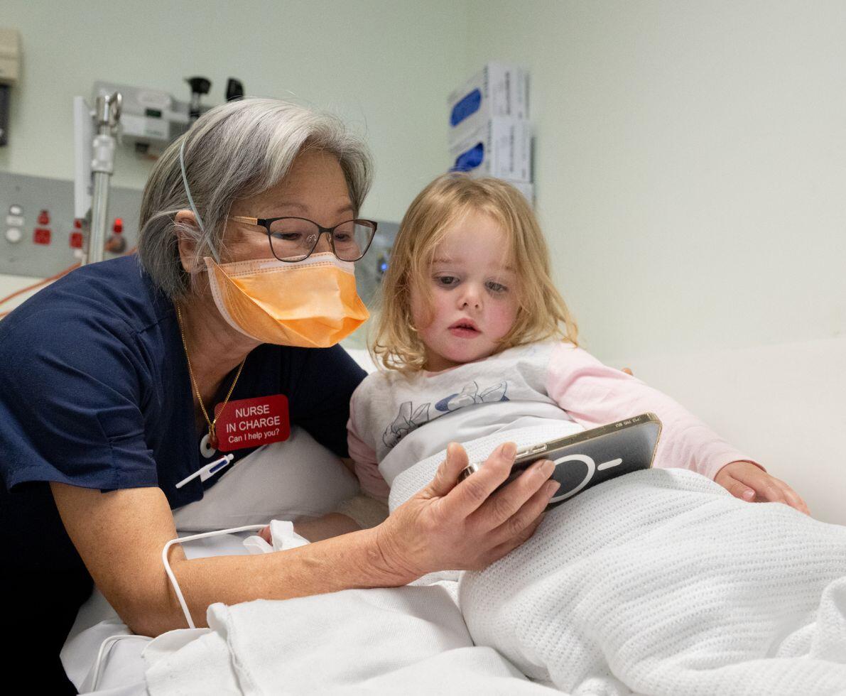 image of a healthcare professional in a hospital setting showing a young patient something on a mobile phone